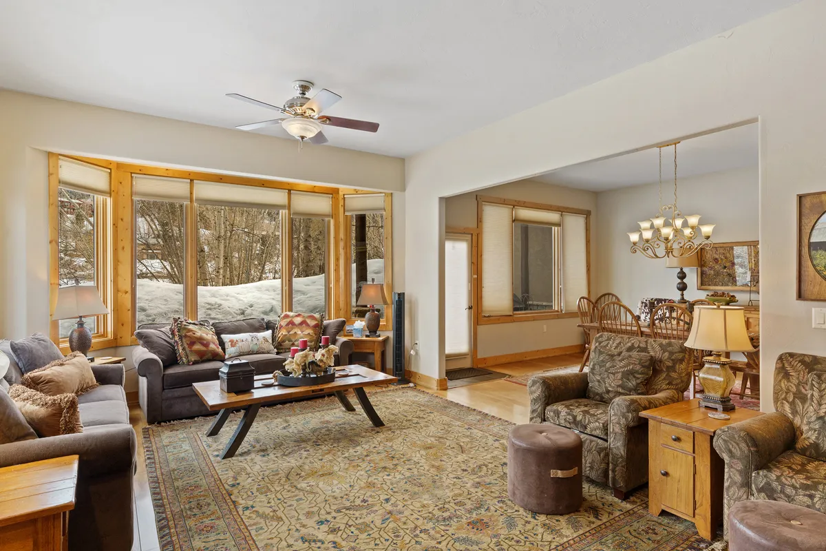 A seating area with panoramic views of a snow-covered mountain landscape through expansive windows. The comfortable furnishings invite relaxation and togetherness, with the adjoining dining area visible, highlighting the open and interconnected layout.