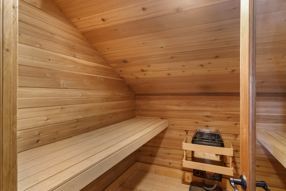 A tranquil sauna space with wooden benches and a heating element, exuding an atmosphere of relaxation and warmth. The setting is designed for unwinding after outdoor adventures, offering a private retreat within the unit.
