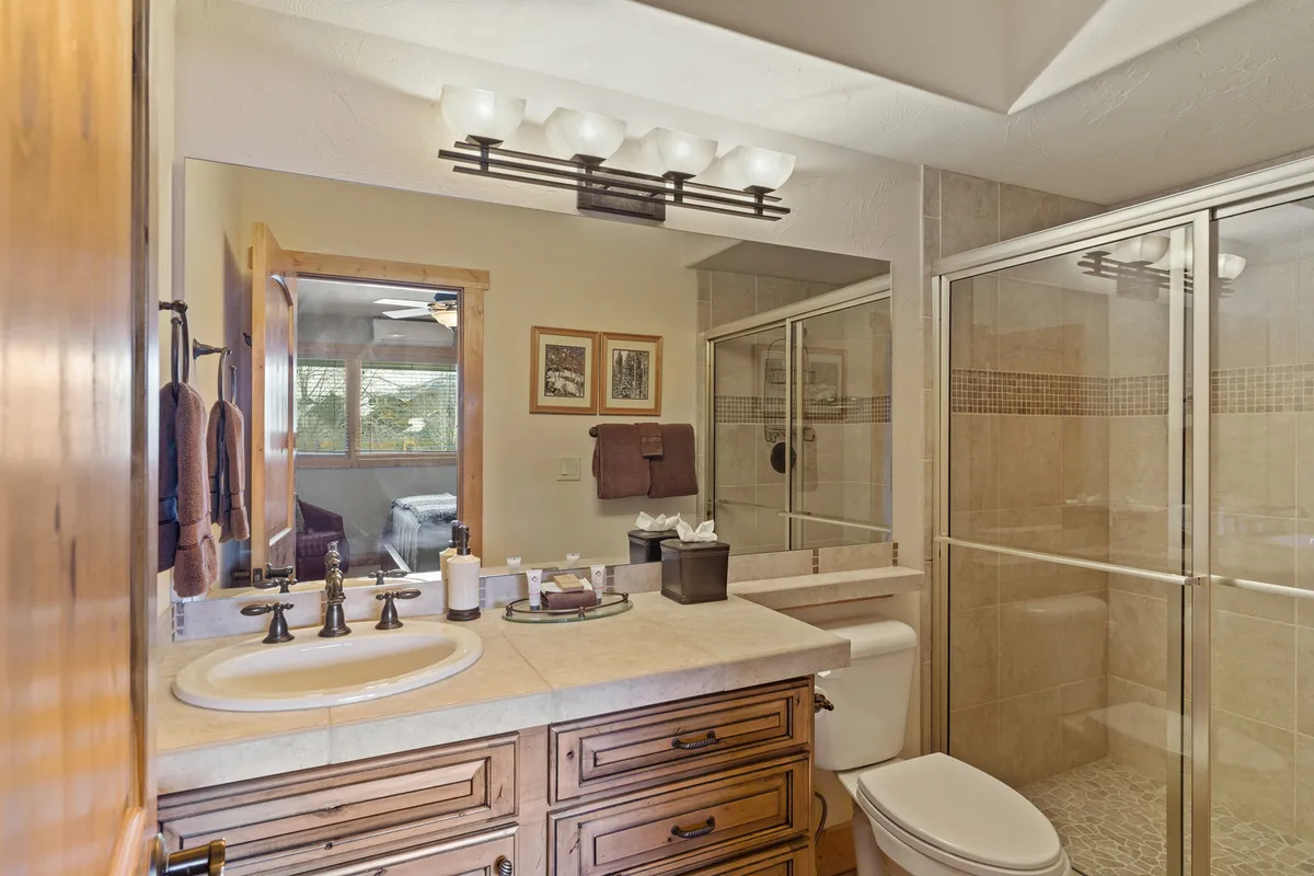 A contemporary ensuite bathroom featuring a wooden vanity, framed artwork, and a glass shower enclosure. The clean lines and calming color palette invite relaxation and privacy, enhancing the comfort of the adjoining bedroom.