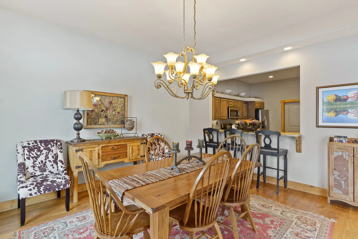 A warmly lit wooden dining table surrounded by decorative chairs sits beneath an elegant chandelier. The sideboard with a lamp adds a touch of hominess, and the inviting setup hints at gatherings, celebrations, and shared meals.