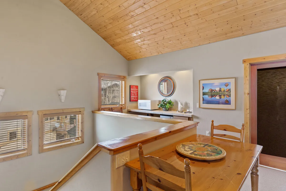 A cozy dining table setup adjoining a kitchen counter, with decorative wall art and a large mirror that expands the sense of space. The arrangement feels casual and sociable, suggesting an area where families naturally gather for food and fun.