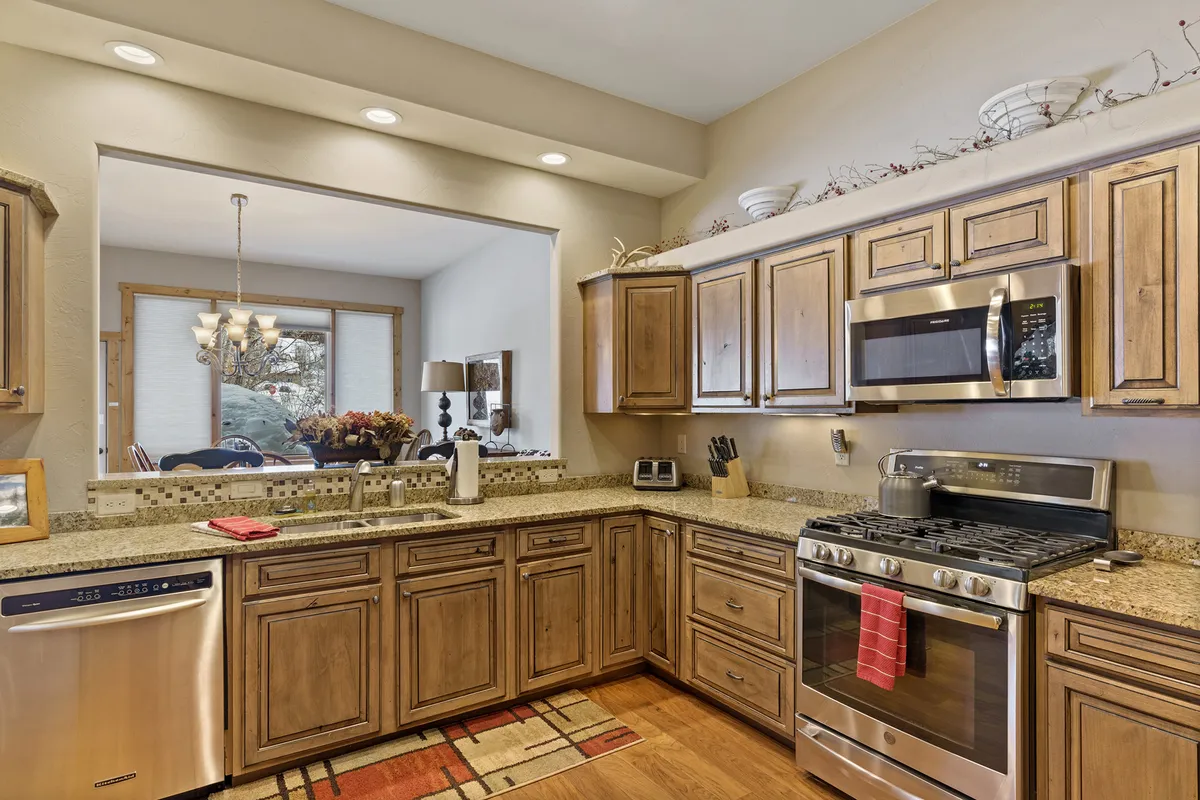 The image showcases a modern kitchen with granite countertops, wooden cabinets, and stainless steel appliances, offering a clear view into the adjoining dining area. The space exudes warmth and functionality, inviting guests to cook, gather, and share meals.